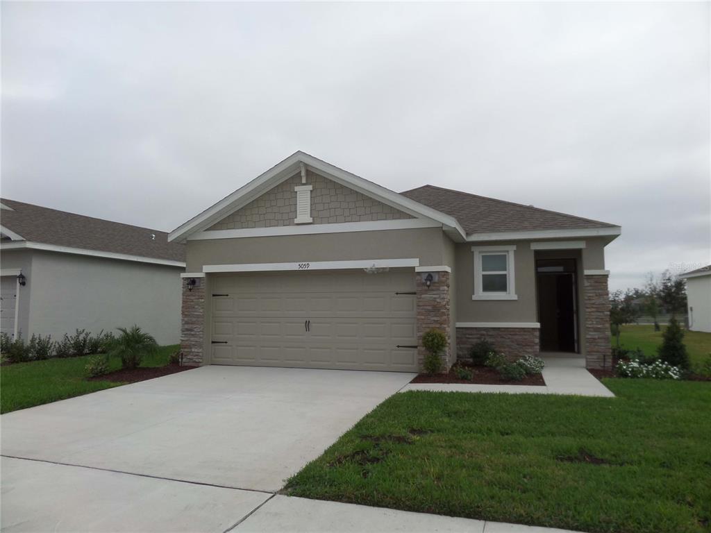 A single-story suburban house with a tan stucco exterior, stone accents, and a two-car garage — 5059 STOKES WAY, WILDWOOD, FL