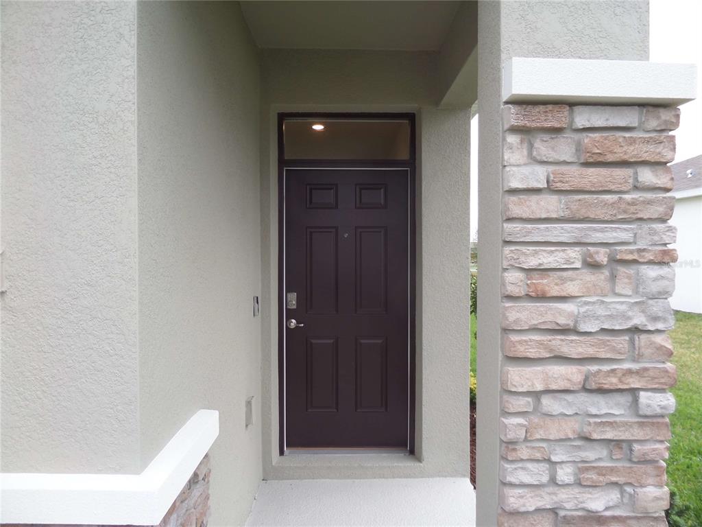 A dark brown front door with a transom window sits under a covered entryway — 5059 STOKES WAY, WILDWOOD, FL