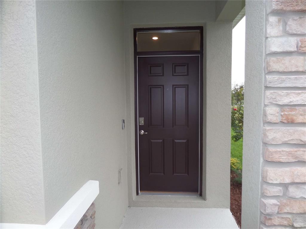 A dark brown front door with a transom window is set within a covered entryway — 5059 STOKES WAY, WILDWOOD, FL