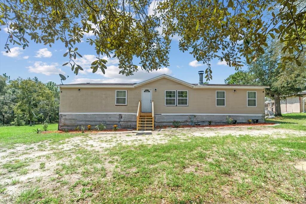 A single-story manufactured home with tan siding and a wooden staircase sits on a lawn — 13120 SW 90TH STREET, DUNNELLON, FL