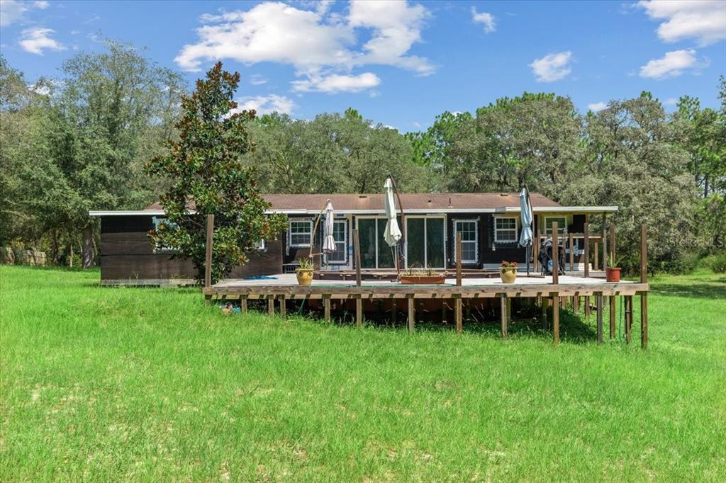 A dark-sided house features a large wooden deck with a pool and patio umbrellas — 13120 SW 90TH STREET, DUNNELLON, FL