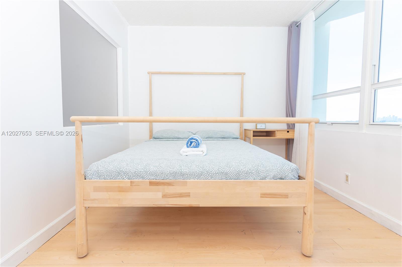 A bedroom features a light wood bed frame, light-colored wood flooring, and large windows — 5445 Collins Ave # 1105, Miami Beach FL 33140, MIAMI BEACH, FL