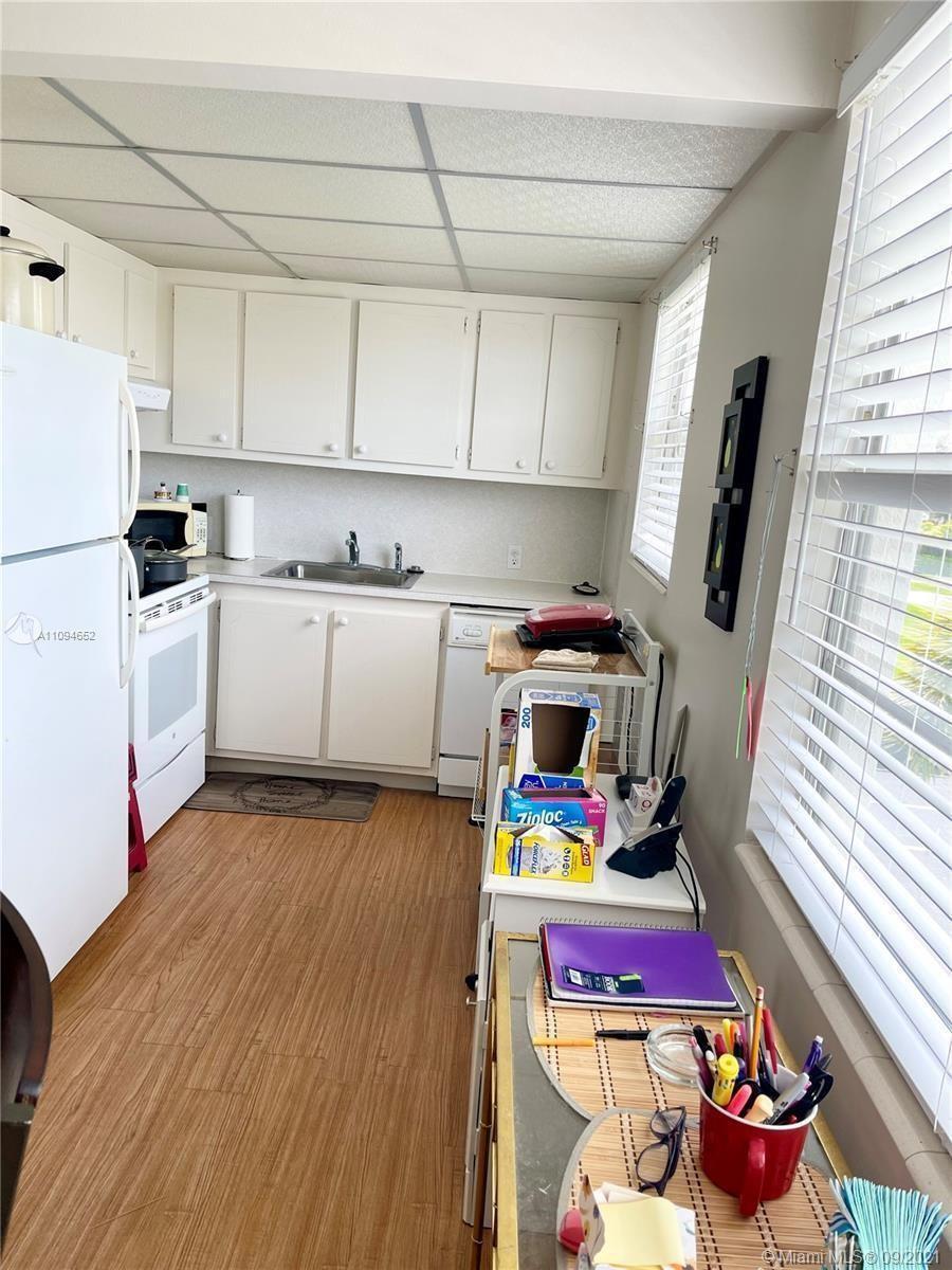 A small kitchen features white cabinets, a white refrigerator, and wood-look flooring — 84 Brighton B # 84, Boca Raton FL 33434, BOCA RATON, FL