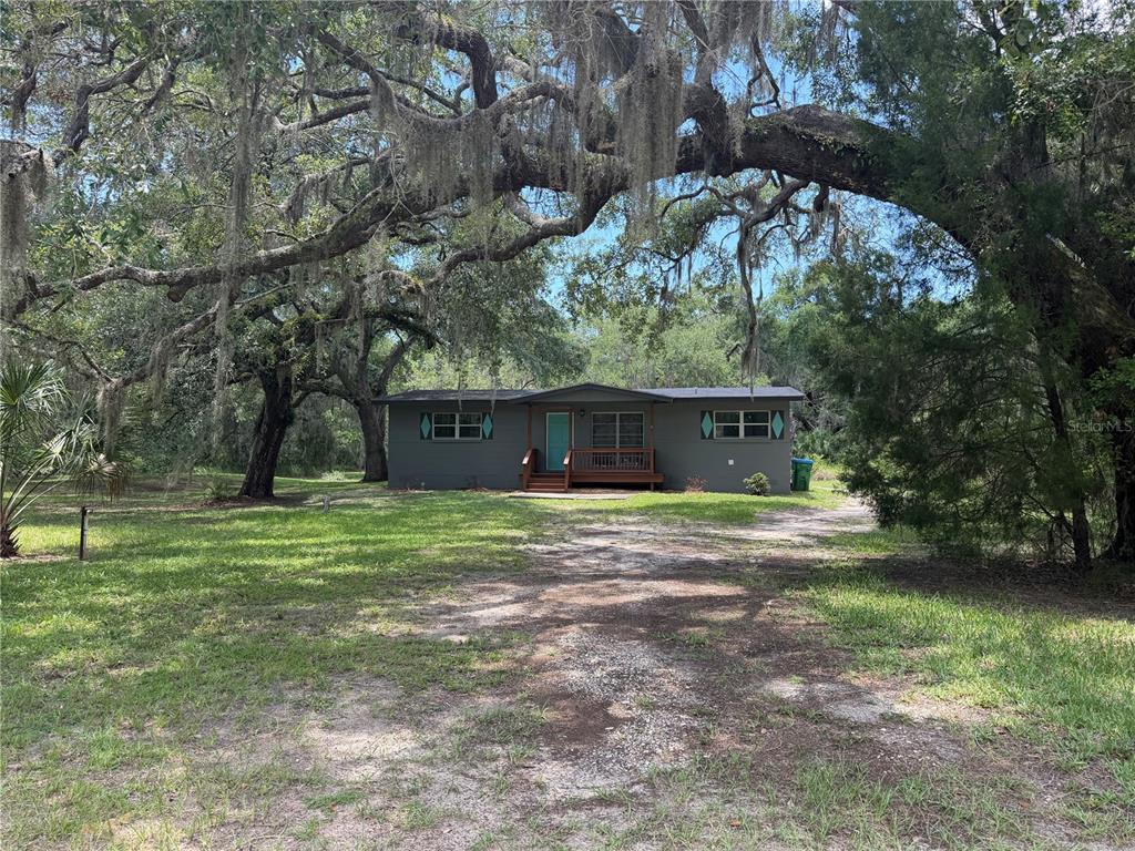 A gray single-story house with a wooden porch sits among large trees with Spanish moss — 8668 N ELMTREE AVENUE, CRYSTAL RIVER, FL