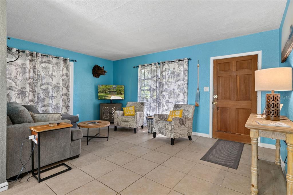 A living room features blue walls, tile flooring, two patterned armchairs, and a wooden door — 8668 N ELMTREE AVENUE, CRYSTAL RIVER, FL