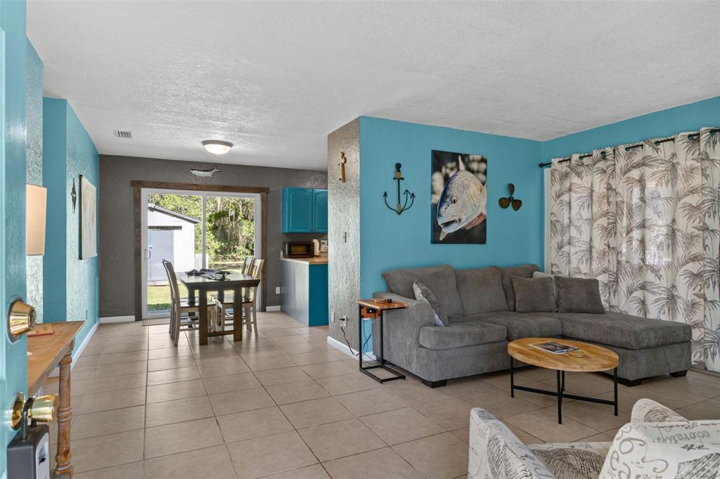 A living room with a gray sectional sofa, tiled floors, and a dining area beyond — 8668 N ELMTREE AVENUE, CRYSTAL RIVER, FL