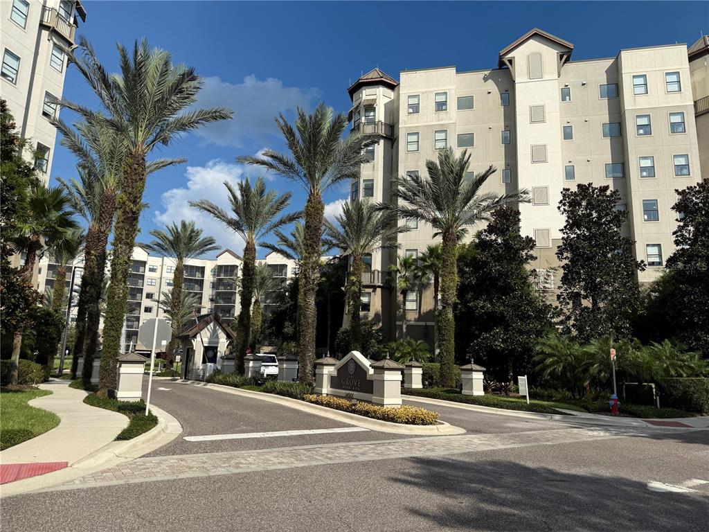 A multi-story resort building stands behind a gated entrance with palm trees and landscaping — 14501 GROVE RESORT AVE UNIT 1622, WINTER GARDEN, FL