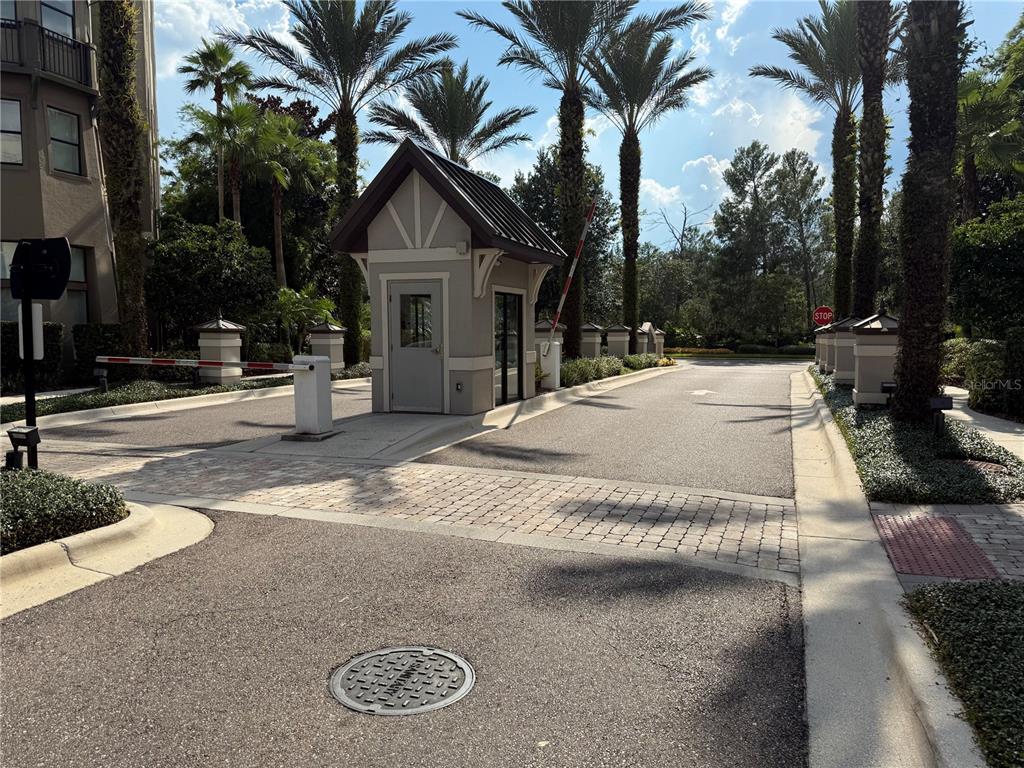A gated entrance with a small guardhouse, palm trees, and a paved driveway — 14501 GROVE RESORT AVE UNIT 1622, WINTER GARDEN, FL
