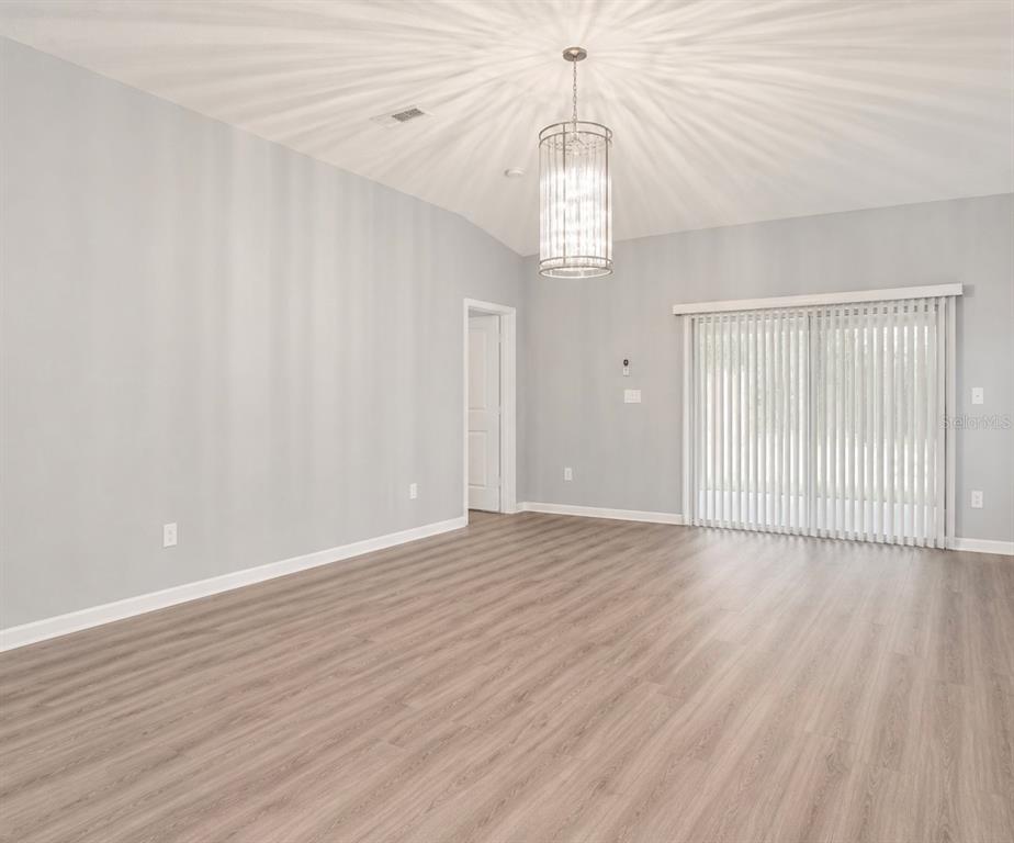 A spacious room with light gray walls, wood-look flooring, a crystal chandelier, and sliding doors — 18686 DOBSON DRIVE, HUDSON, FL