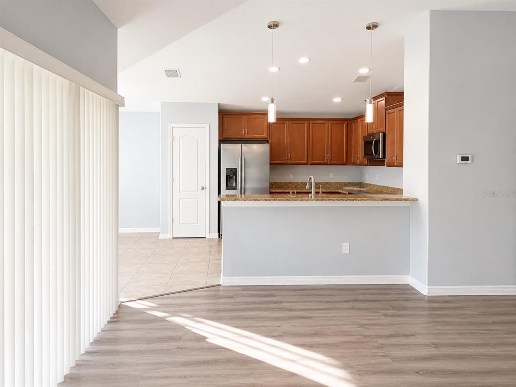 A kitchen with wood cabinets and granite countertops overlooks a living area with wood flooring — 18686 DOBSON DRIVE, HUDSON, FL
