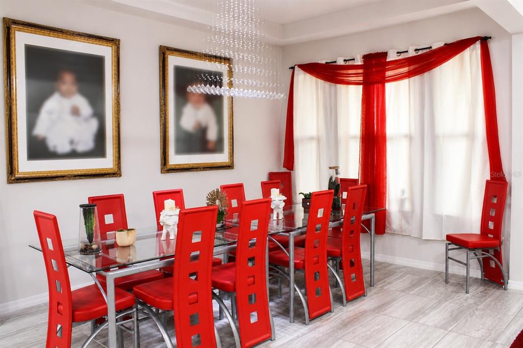 A dining room features a glass table, red chairs, a crystal chandelier, and two framed portraits — 14779 MCCLANE ROAD, WINTER GARDEN, FL