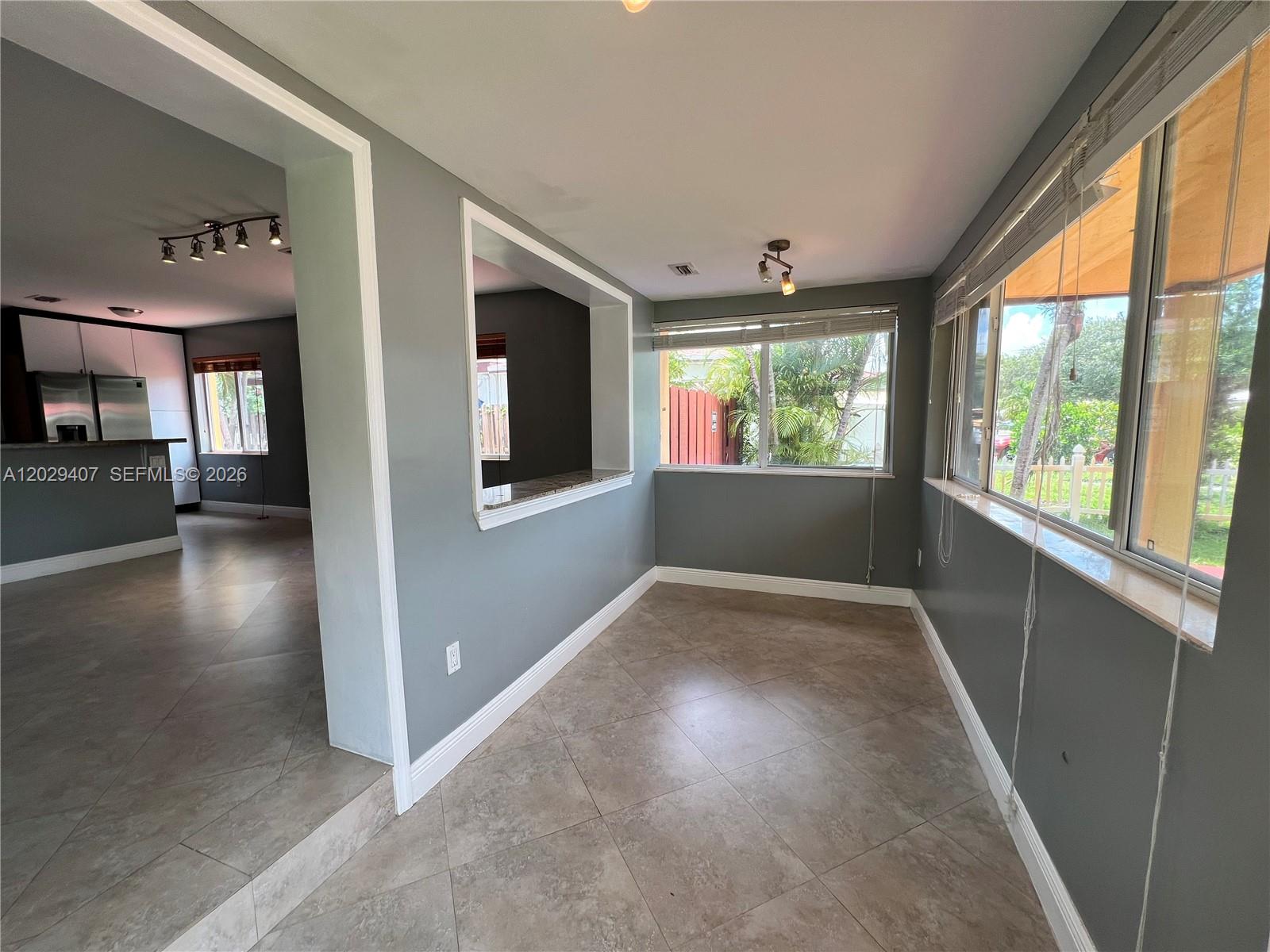 A sunroom with gray walls and tile flooring features a pass-through window to the kitchen — 2502 Dewey St, Hollywood FL 33020, HOLLYWOOD, FL