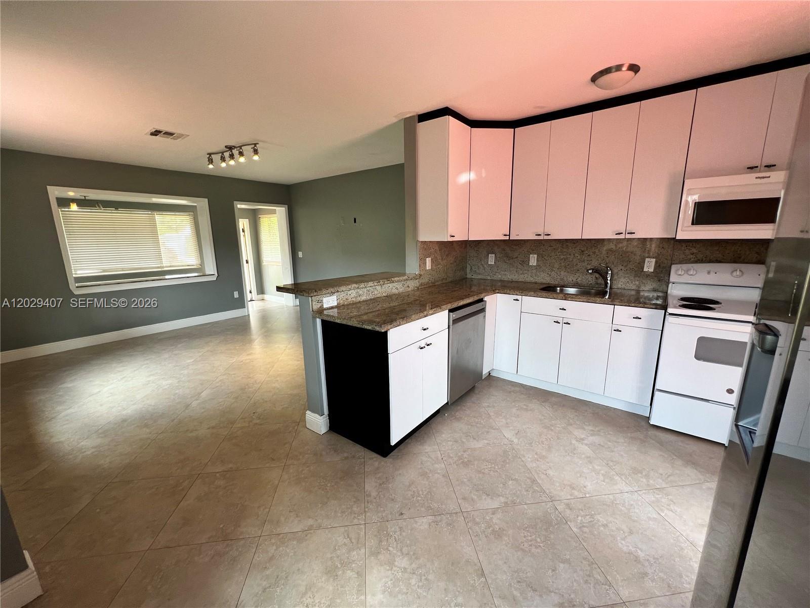 A kitchen with white cabinets and granite countertops opens into a living area with tile — 2502 Dewey St, Hollywood FL 33020, HOLLYWOOD, FL