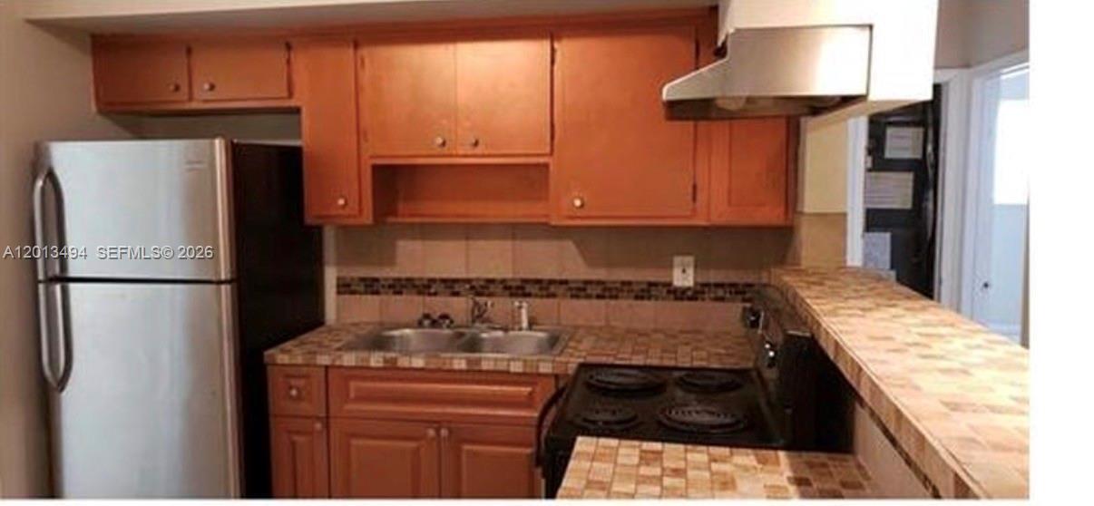 A kitchen features wooden cabinets, a stainless steel refrigerator, a black stove, and tiled countertops — 5631 SW 27th St, West Park FL 33023, WEST PARK, FL