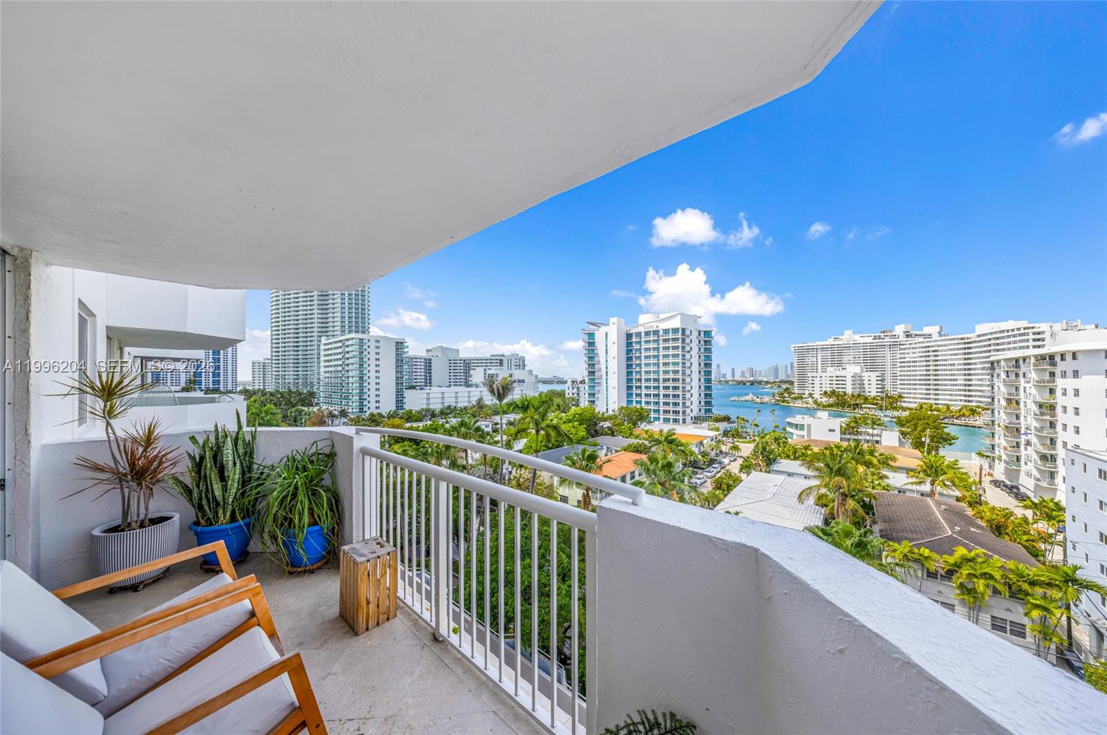 A balcony with chairs and potted plants overlooks a city skyline and a bay — 1621 Bay Rd # 802, Miami Beach FL 33139, MIAMI BEACH, FL