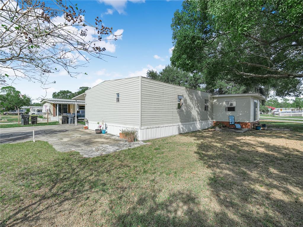 A side view of a light-colored mobile home with a concrete patio and grassy yard — 319 1ST AVENUE N, LAKE WALES, FL