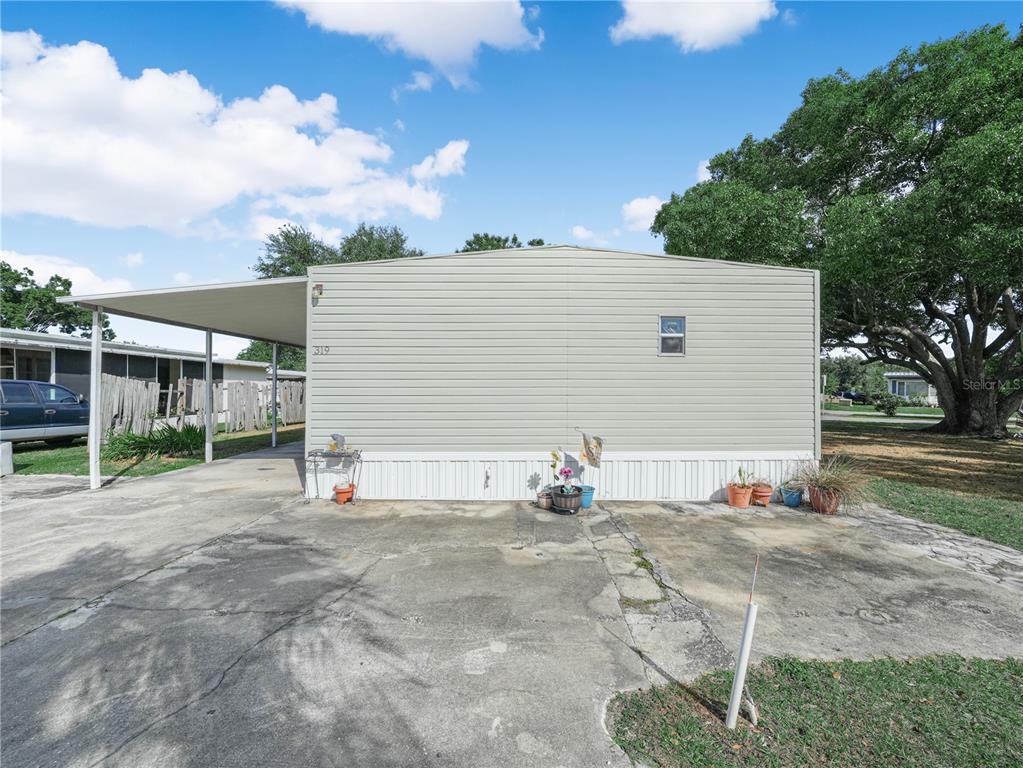 A light-colored mobile home with a carport and a concrete driveway under a blue sky — 319 1ST AVENUE N, LAKE WALES, FL