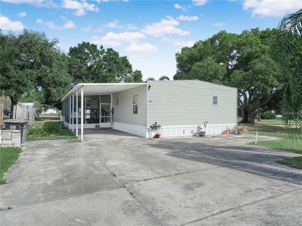 A light-colored mobile home features a concrete driveway and a screened-in front porch — 319 1ST AVENUE N, LAKE WALES, FL