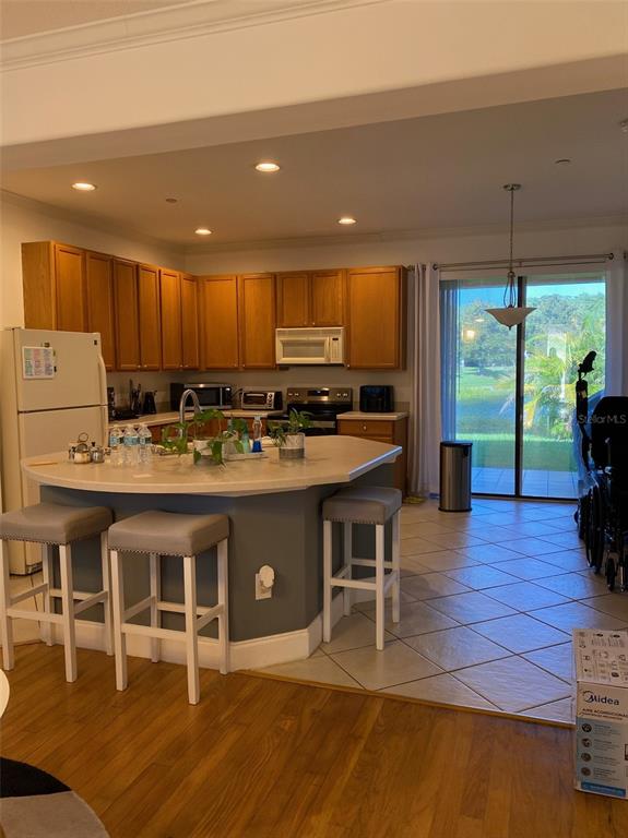A kitchen features wood cabinets, a curved island with bar stools, and a sliding glass door — 10076 SILVER LAUREL WAY, ORLANDO, FL