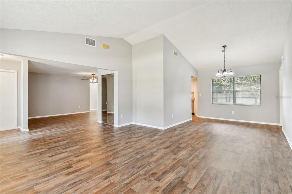 An open-concept living and dining area features vaulted ceilings, light gray walls, and wood-look flooring — 1010 RIFLECREST AVENUE, VALRICO, FL