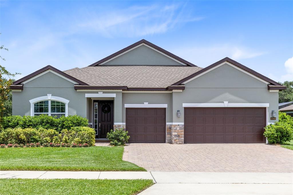 A bright, open-concept living and dining area features white walls, dark wood-look tile flooring, and large windows — 1743 FULLERS OAK LOOP, WINTER GARDEN, FL
