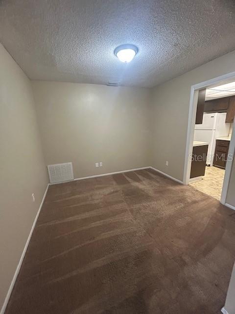 An empty room with beige walls, brown carpet, and a view into a kitchen — 1509 CARDINAL STREET, LONGWOOD, FL
