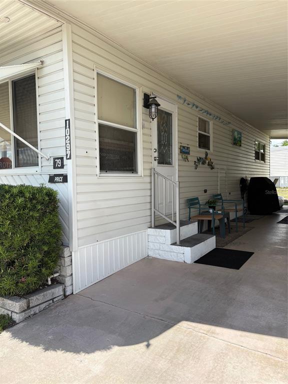 The exterior of a mobile home features a concrete carport, white siding, and front steps — 10297 N LAKE DRIVE UNIT 79, LARGO, FL