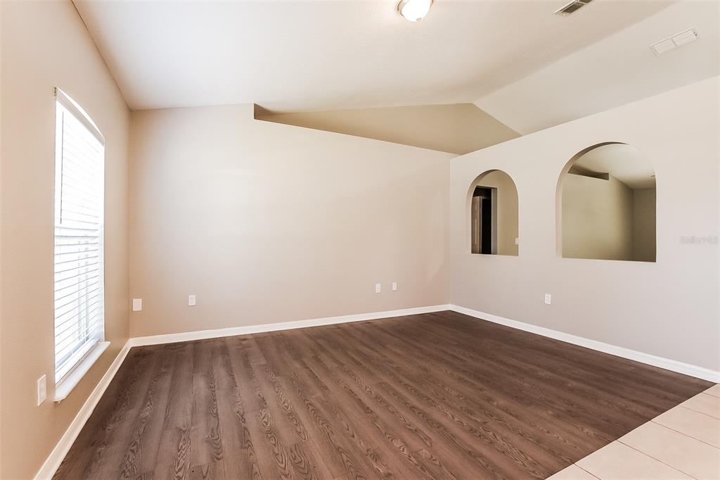 An empty room features dark wood-look flooring, beige walls, and two arched wall niches — 949 CASCADES PARK TRAIL, DELAND, FL
