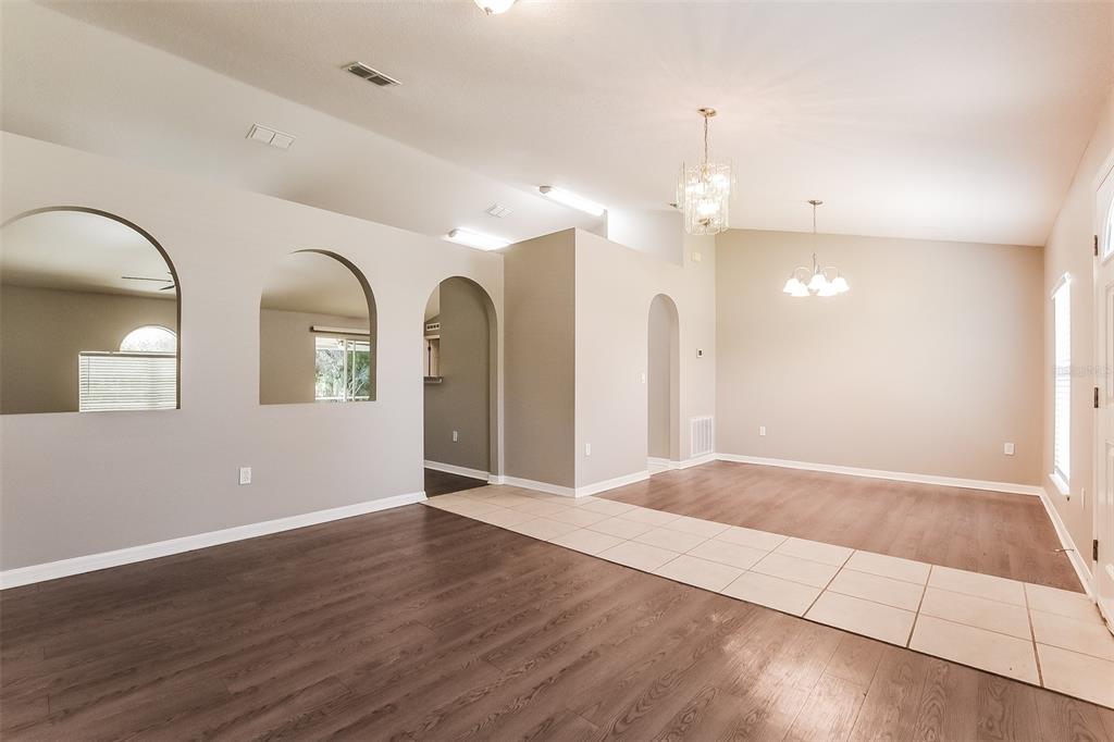 An open-concept living and dining area features arched wall cutouts, tile flooring, and wood-look planks — 949 CASCADES PARK TRAIL, DELAND, FL
