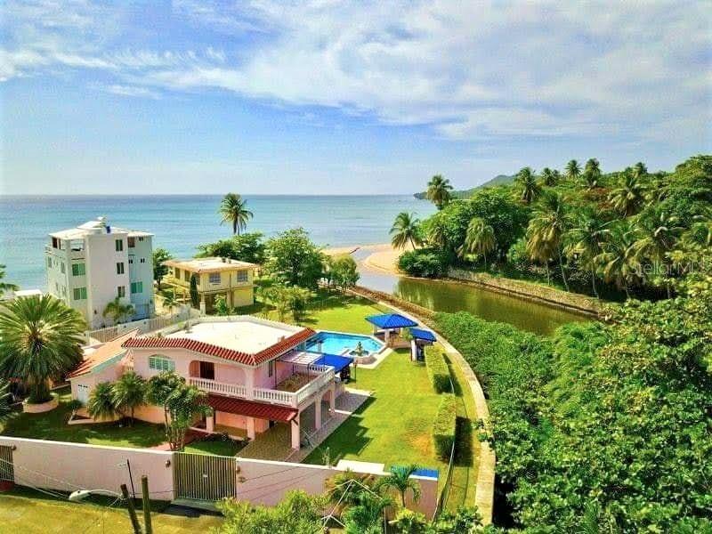 An aerial view shows a pink house with a pool near a river and beach — 23 CASA CANAL, RINCON, PR