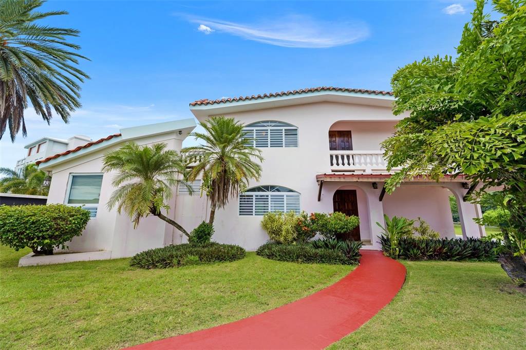 A two-story pink stucco house features a red walkway, palm trees, and a balcony — 23 CASA CANAL, RINCON, PR