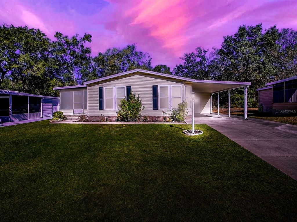 A single-story house with light siding, a carport, and a lawn under a purple sky — 518 SAINT ANDREWS BOULEVARD, LADY LAKE, FL