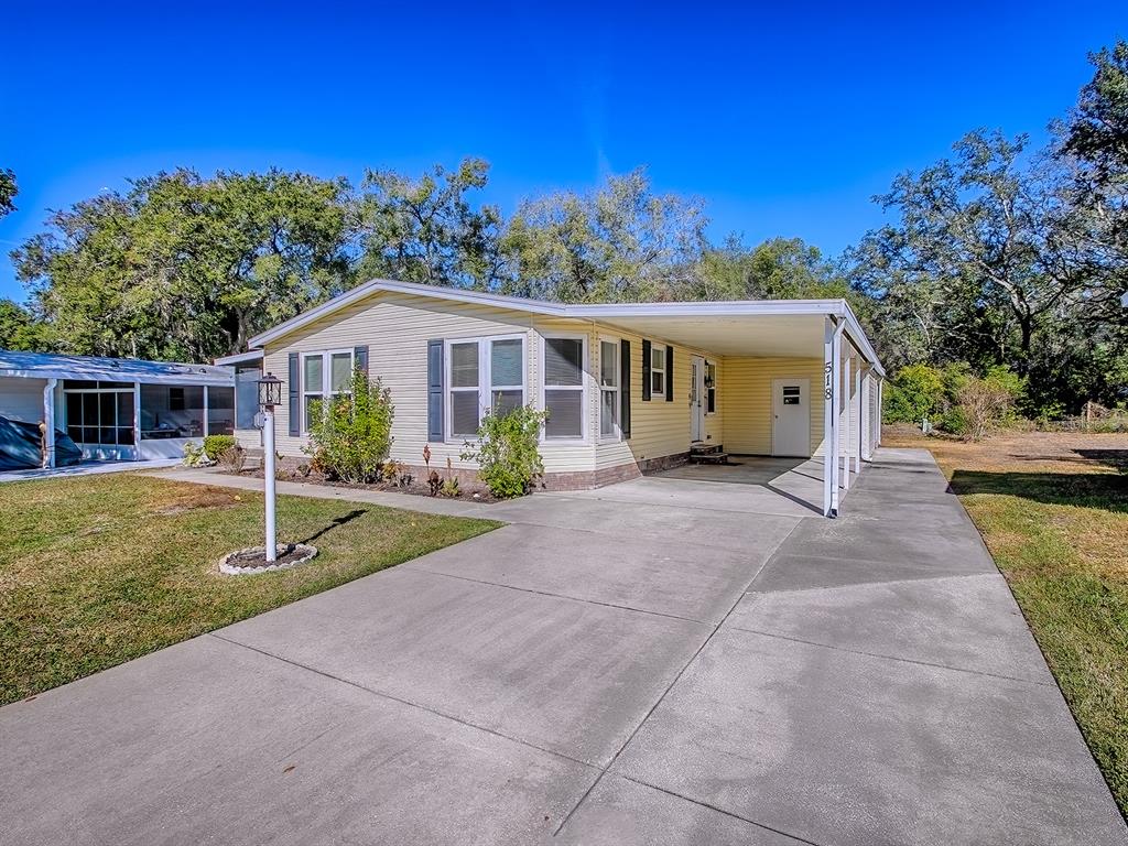 A single-story mobile home with yellow siding, a concrete driveway, and a covered carport — 518 SAINT ANDREWS BOULEVARD, LADY LAKE, FL