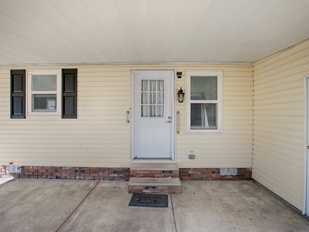 A beige vinyl-sided house exterior features a white front door, two windows, and concrete steps — 518 SAINT ANDREWS BOULEVARD, LADY LAKE, FL