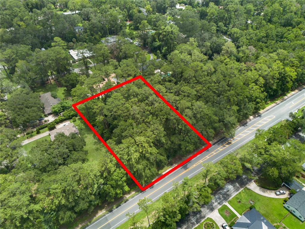 An aerial view shows a rectangular, tree-covered vacant lot outlined in red next to a road — 0000 NW 34TH STREET, GAINESVILLE, FL