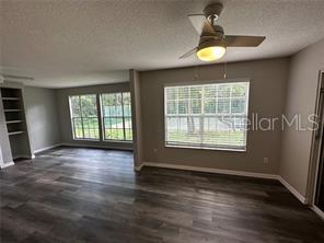 A living room with wood-look flooring, a ceiling fan, and large windows overlooking a tennis court — 713 SANDY COURT UNIT 375, ALTAMONTE SPRINGS, FL