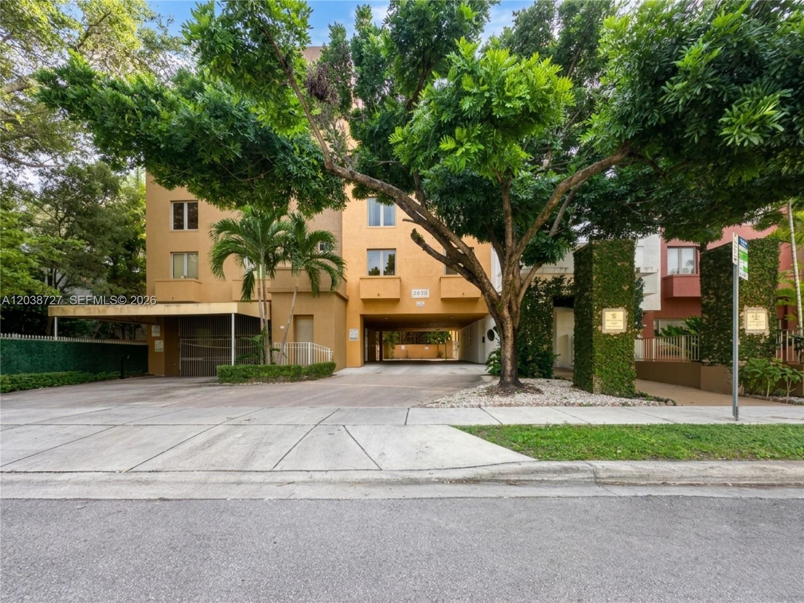 A multi-story tan apartment building features a covered driveway entrance and mature shade trees — 2630 SW 28th St # 44, Miami FL 33133, MIAMI, FL