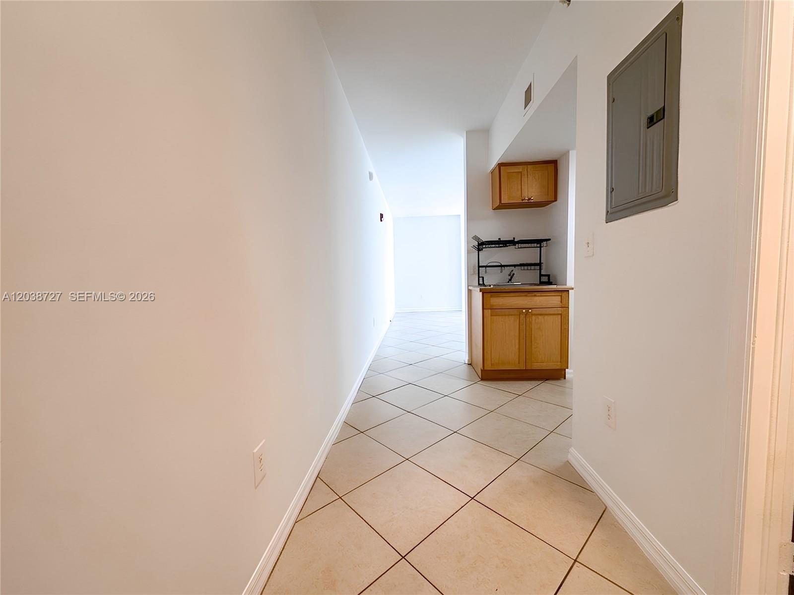 A hallway with tiled floors leads to a small kitchen area with wooden cabinets — 2630 SW 28th St # 44, Miami FL 33133, MIAMI, FL