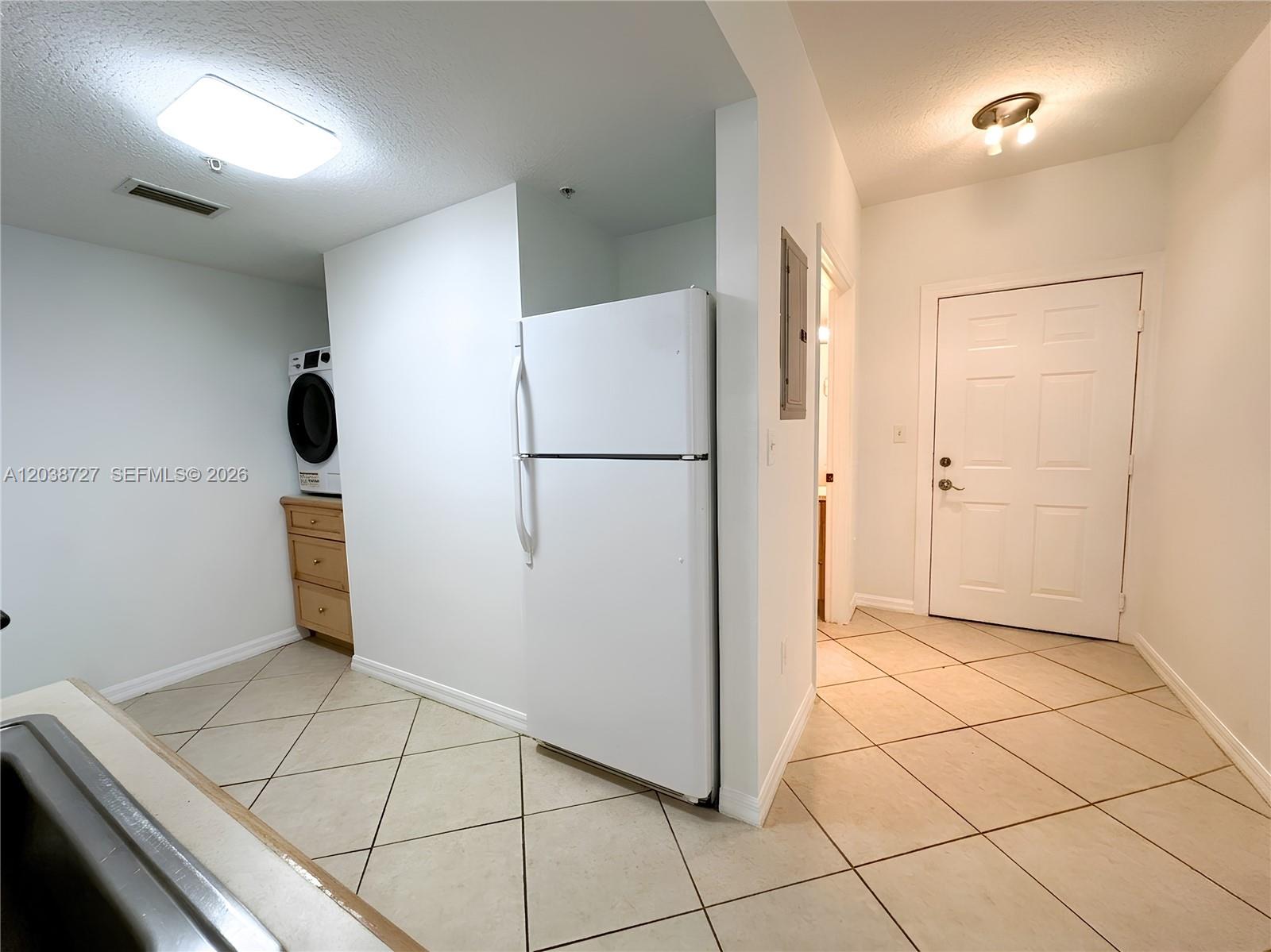 A kitchen area features a white refrigerator, a stacked washer-dryer, and tiled flooring — 2630 SW 28th St # 44, Miami FL 33133, MIAMI, FL