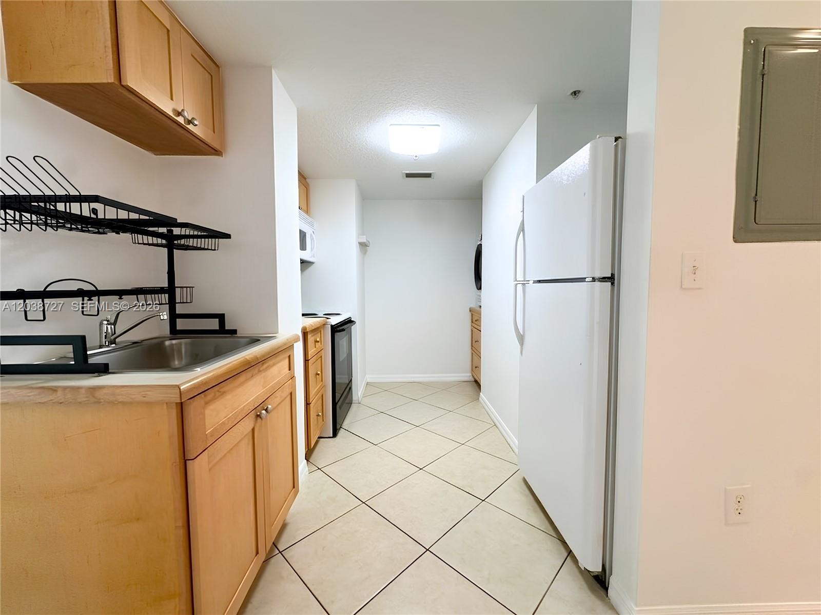 A galley kitchen features light wood cabinets, a white refrigerator, and beige tile flooring — 2630 SW 28th St # 44, Miami FL 33133, MIAMI, FL