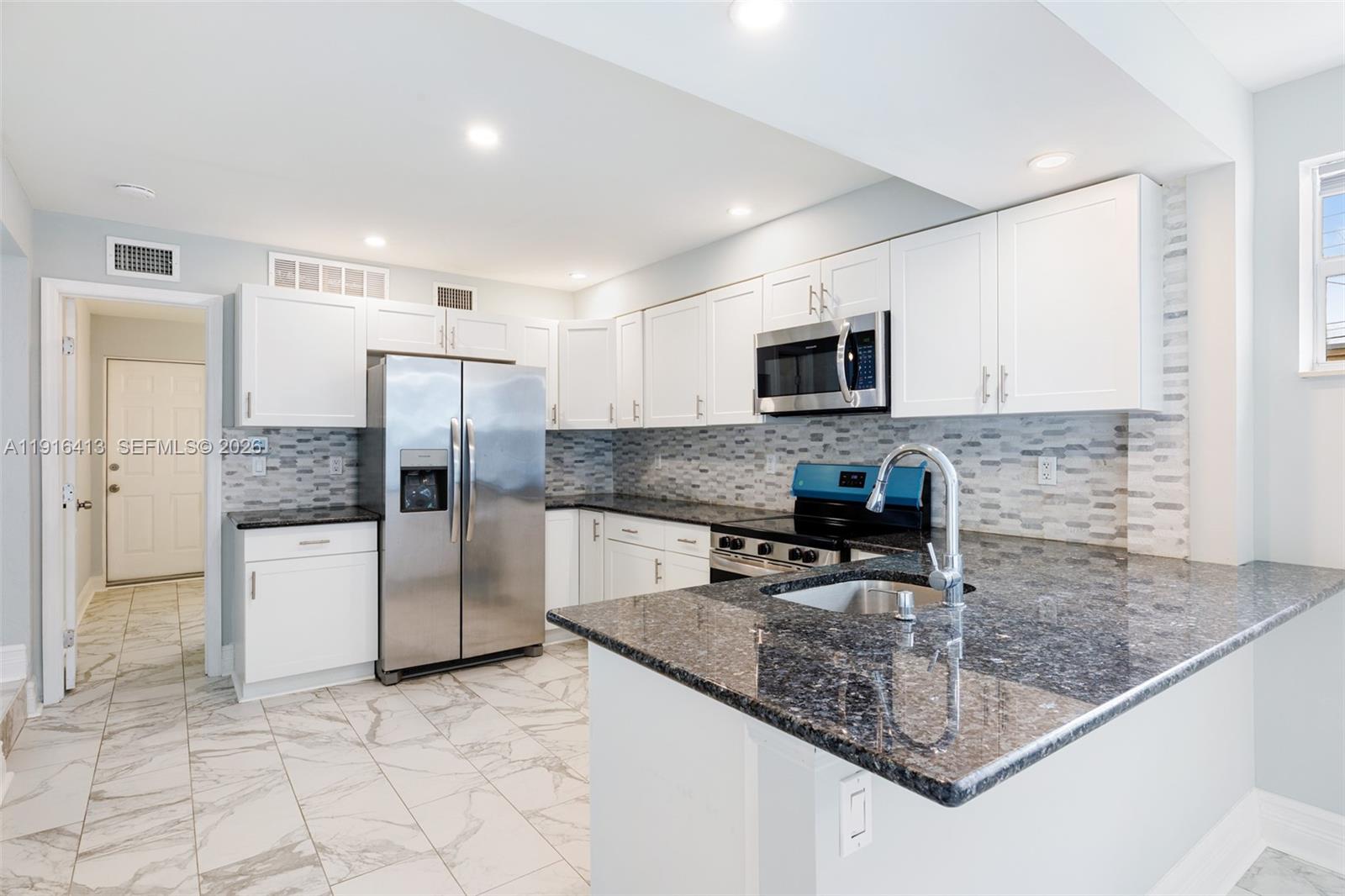 A kitchen features white cabinets, granite countertops, stainless steel appliances, and light-colored tile flooring — 112 Milton St # 112, Lantana FL 33462, LANTANA, FL