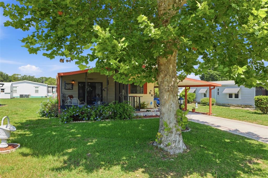 A single-story mobile home with a screened porch and attached carport sits behind a tree — 409 TIVOLI PARK DRIVE, DAVENPORT, FL