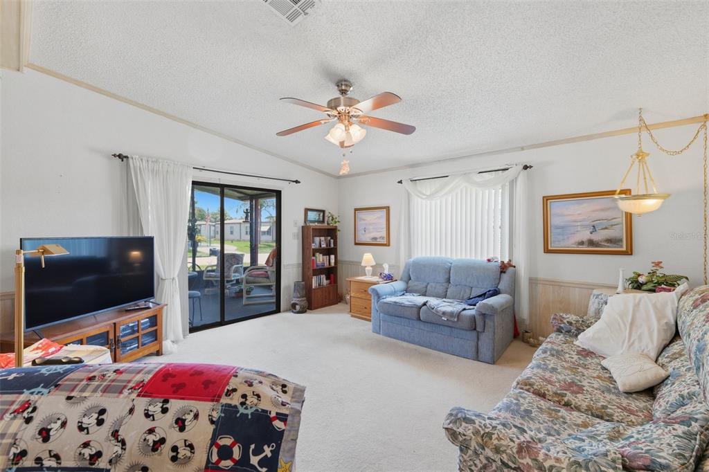 A living room features a ceiling fan, sliding glass doors, and two sofas on carpet — 409 TIVOLI PARK DRIVE, DAVENPORT, FL