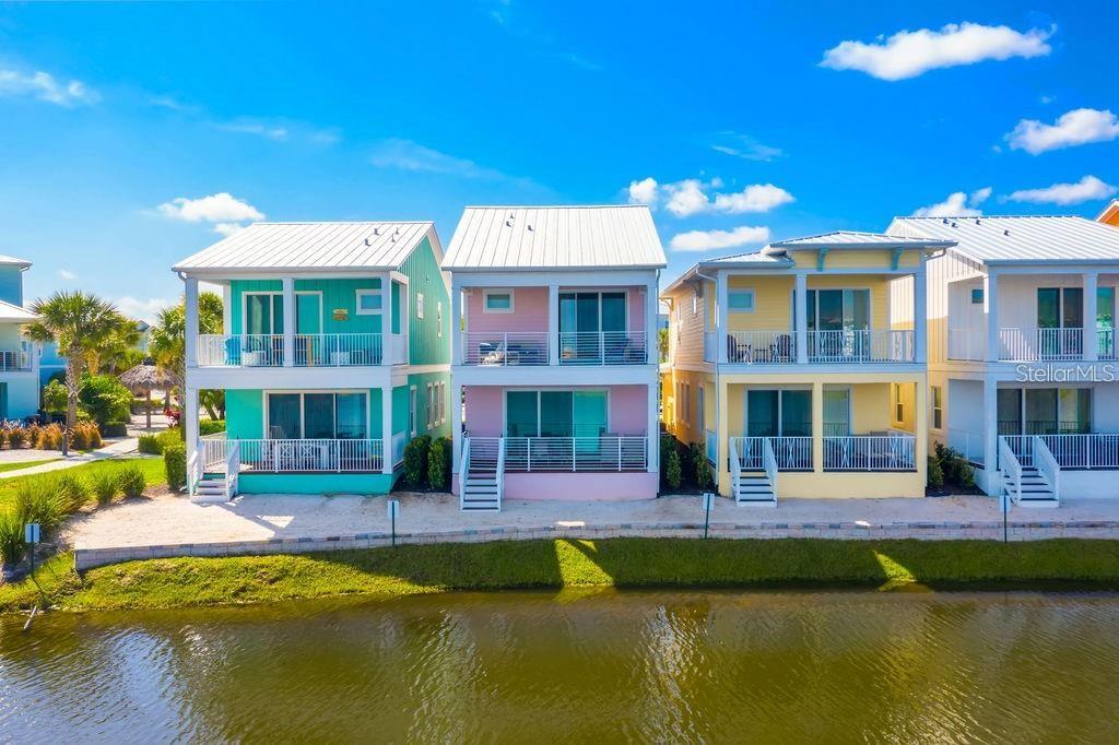 Four colorful, multi-story coastal houses stand in a row along a waterfront canal — 8117 SURF STREET, KISSIMMEE, FL