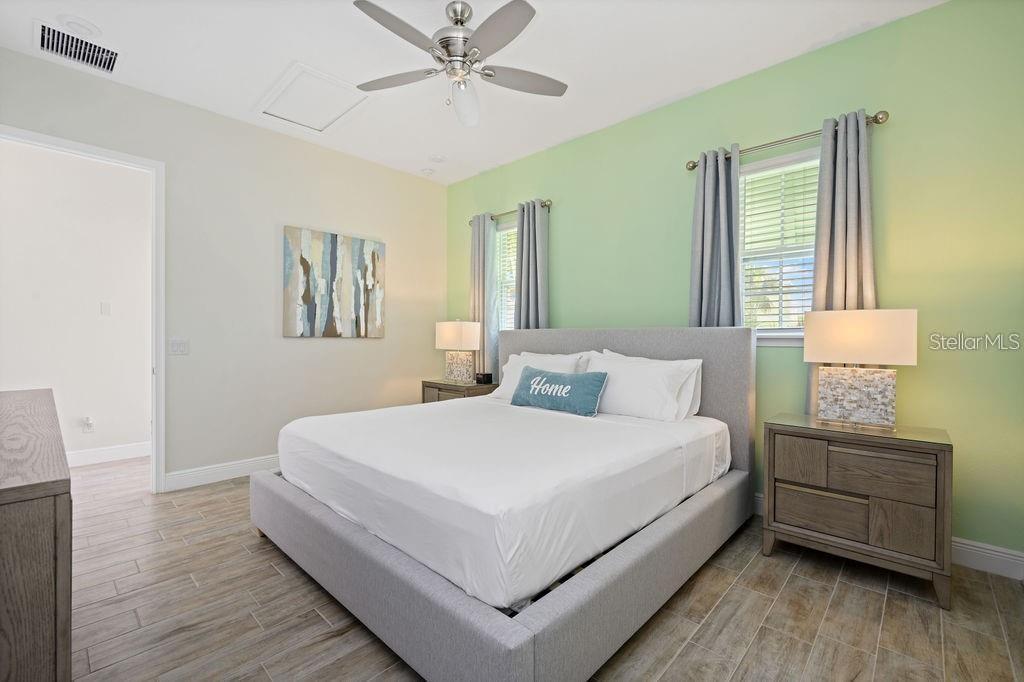 A bedroom features a gray upholstered bed, light green accent wall, and wood-look tile flooring — 8117 SURF STREET, KISSIMMEE, FL