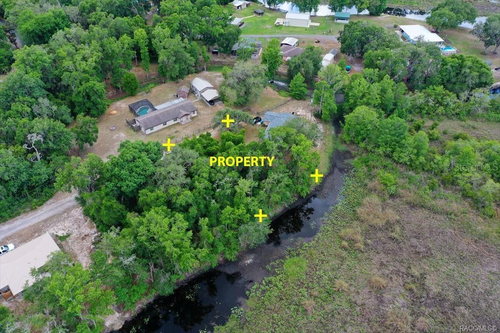 An aerial view shows a wooded property with a house and pool near a creek — 6979 E GRASS COURT, INVERNESS, FL