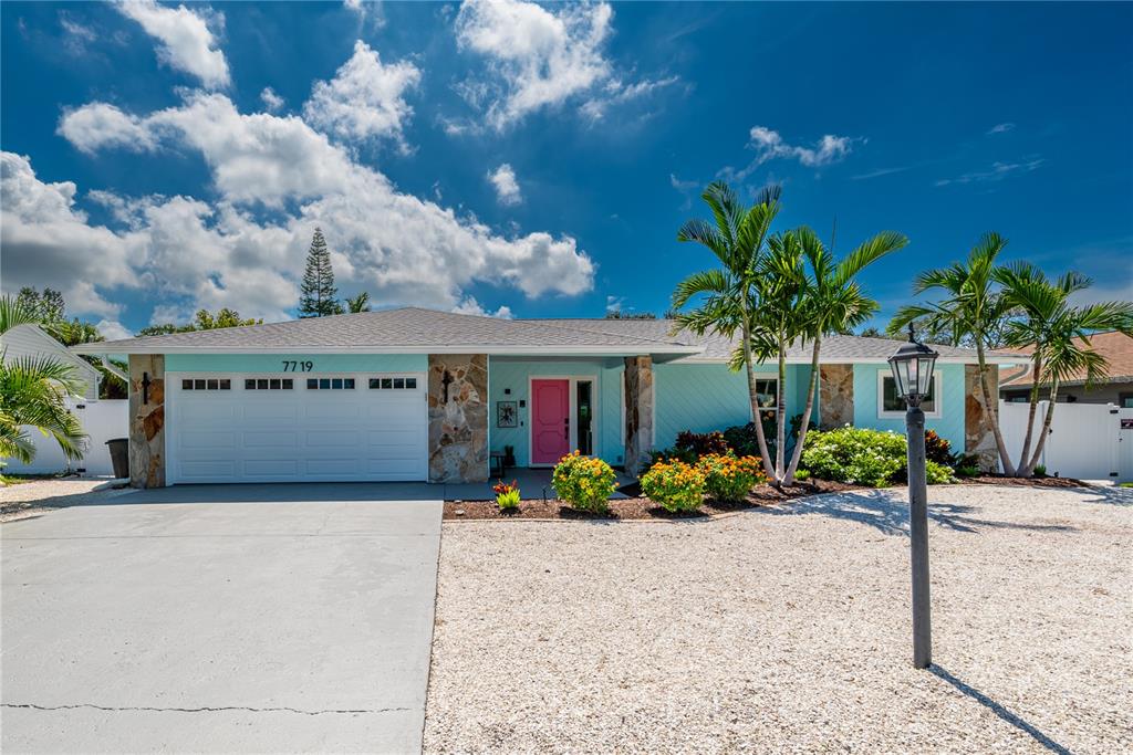 A light blue single-story house features a pink front door, stone accents, and palm trees — 7719 25TH AVENUE W, BRADENTON, FL