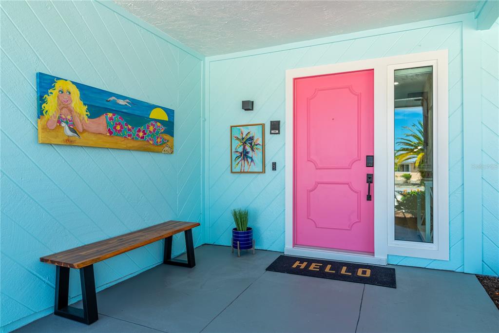 A bright blue porch features a pink front door, a wooden bench, and wall art — 7719 25TH AVENUE W, BRADENTON, FL