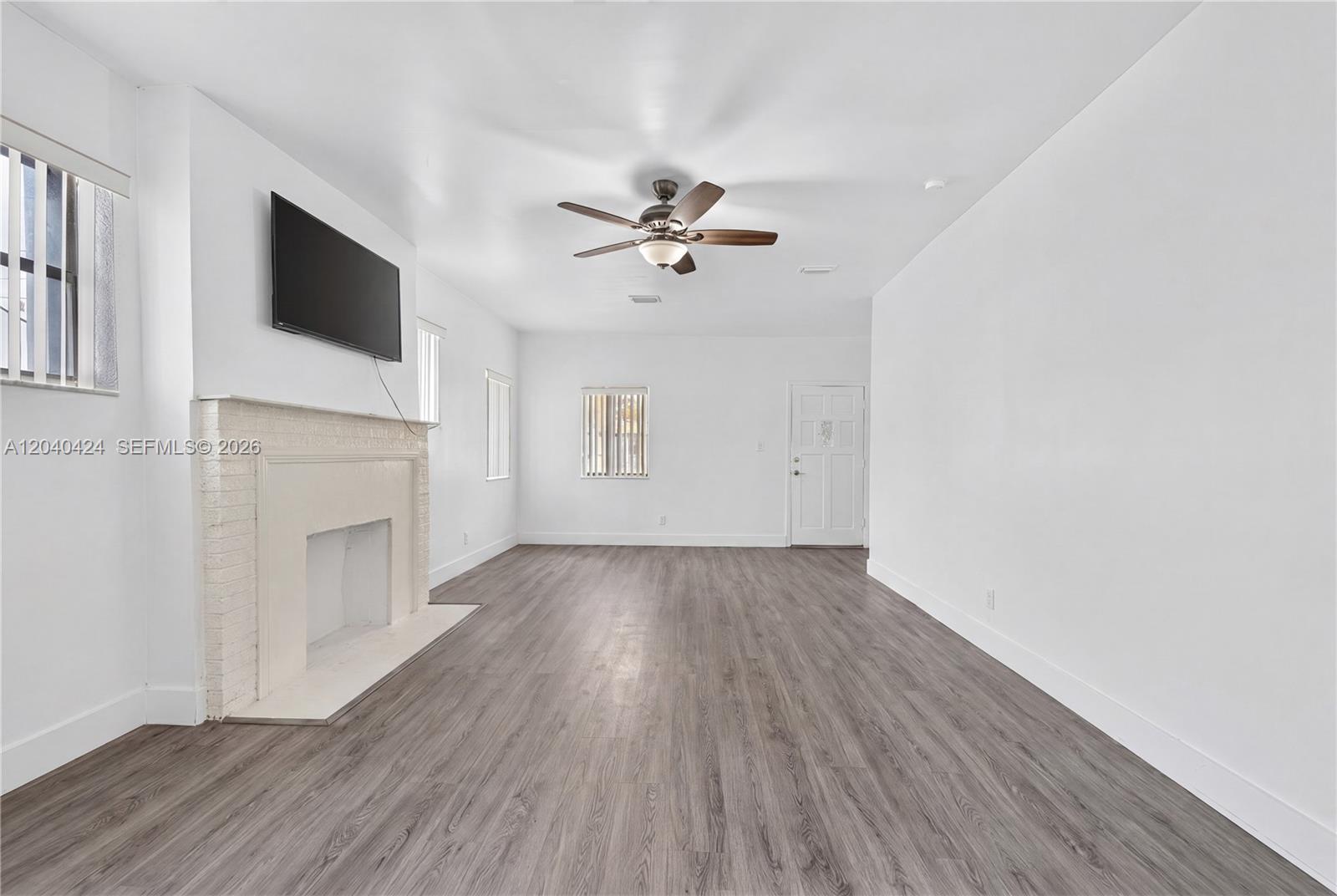 A living room features white walls, wood-look flooring, a ceiling fan, and a brick fireplace — 1168 NW 30th St # 1168, Miami FL 33127, MIAMI, FL