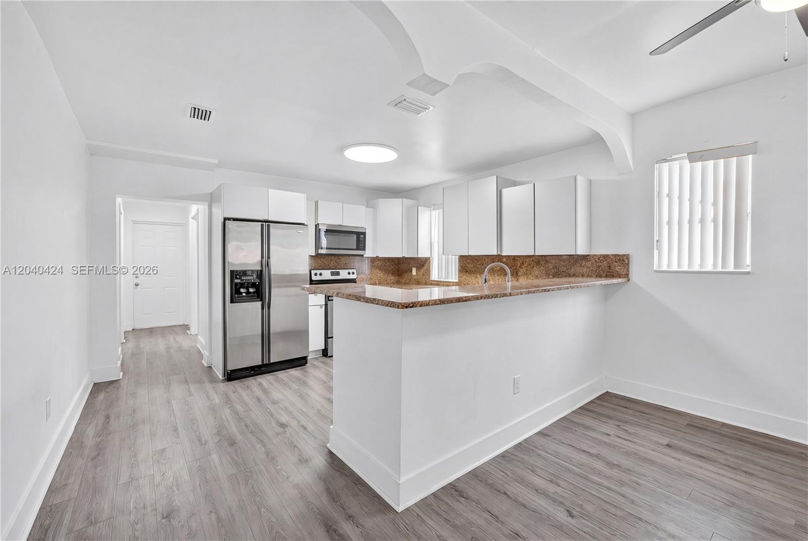 A kitchen features white cabinets, stainless steel appliances, and a granite-topped breakfast bar — 1168 NW 30th St # 1168, Miami FL 33127, MIAMI, FL